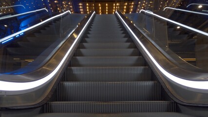 Close up of upward moving stairs with white lights on sides in business and shopping centre with no people around 