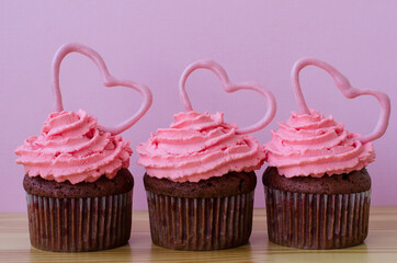 Muffin decorated with pink cream and hearts on a wooden background. Valentine's day gift. Romance. Red velvet cupcake.