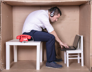 businessman in a cramped cardboard office trying to focus on his work