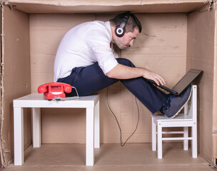 businessman in a cramped cardboard office trying to focus on his work