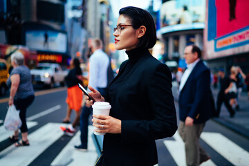 Stylish businesswoman with coffee and cellphone on crosswalk