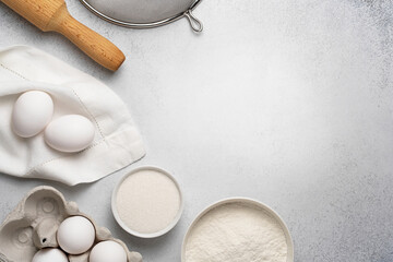 Wheat flour, sugar, sieve, rolling pin and white eggs on napkin on grey background. Flat lay with baking ingredients for dough. Top view, copy space.