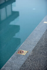Fototapeta premium No diving sign on a pool side for a shallow pool with a reflection showing a modern building; hotel or condominium, in a peaceful turquoise color scheme during the morning time.