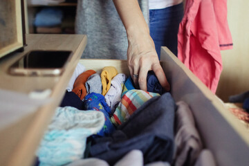 A woman is sorting through things in her home wardrobe with her hands. Folding clothes after...
