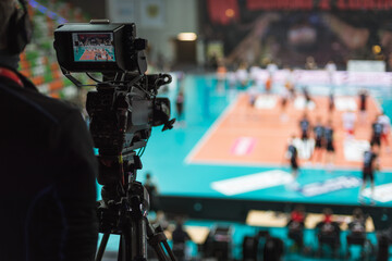 Professional TV camera with volleyball match in the background.