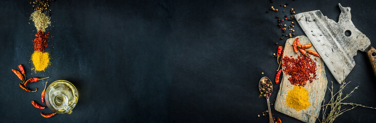 Colourful spices and herbs with old kitchen axe on black table, top view with copy space