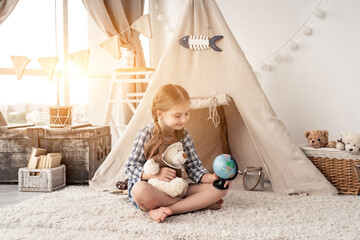 Little girl exploring globe with teddy bear sitting in wigwam in playroom © Ievgen Skrypko