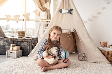 Little girl with teddy bear and globe sitting in wigwam settled in playroom © Ievgen Skrypko