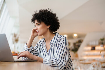 Beautiful focused curly woman working with laptop while sitting in cafe