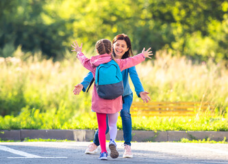 Fototapeta premium Mother meeting schoolgirl after lessons on sunny car parking