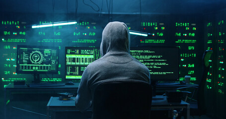 Rear view of incognito hacker using computer for organizing massive data breach attack on corporate...
