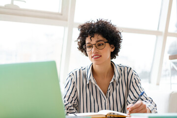 Beautiful happy woman in eyeglasses using laptop while working in cafe