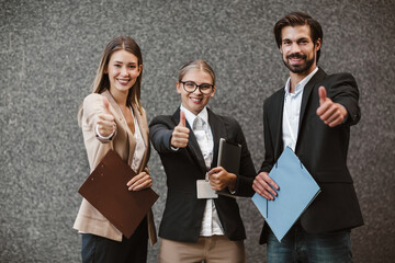Office colleagues talking outdoors near the office building, discussing new project, holding clipboard and digital tablet, showing thumbs up.