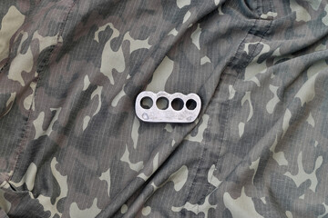 Iron brass cnuckles on crumpled camouflage clothes close up. Football hooliganism and racism concept