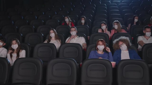 Young audience wearing face masks enjoying time in cinema.