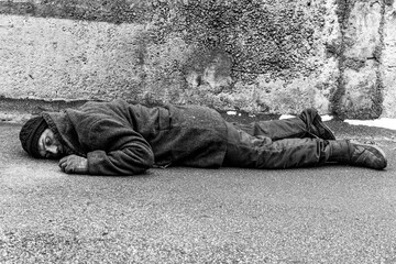 A dirty homeless man lies on the asphalt.