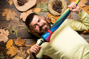 Cheerful man rejoices in autumn sales. Autumn discounts on clothes. man with rainbow color umbrella. He likes rain. weather forecast promises rain. Bearded man holding colorful umbrella
