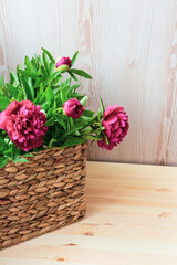 Pink peonies in a wicker basket on a wooden background