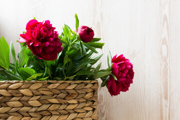 pink red peonies in wicker basket on wooden background