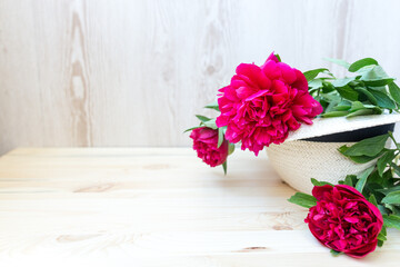 pink red peonies in wicker hat on wooden background