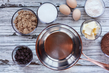 Top view of ingredients for homemade fudgy brownies and sauce pan over a white rustic wooden table. 
