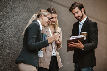 Office colleagues talking outdoors near the office building, discussing new project, holding clipboard and digital tablet.