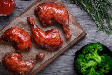 Caramelized chicken legs, cooked broccoli in a cast-iron pan and fresh rosemary on a wooden background. The view from the top.