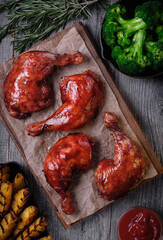 Caramelized chicken legs, grilled potatoes, cooked broccoli in a cast-iron pan, cutchup and fresh rosemary on a wooden background. The view from the top.