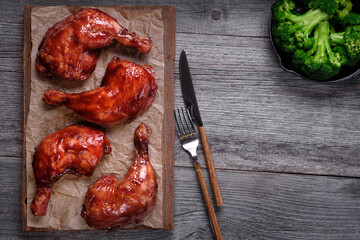 Caramelized chicken legs, grilled potatoes, cooked broccoli in a cast-iron pan, cutchup and fresh rosemary on a wooden background. The view from the top.