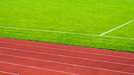 Fototapeta premium Red running track and green grass field on sports stadium.