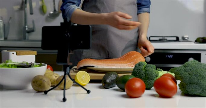 online food courses - woman vloger recording video at home kitchen. showing salmon preparing recipe