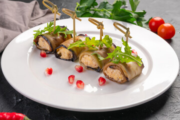 eggplant roll with cheese, arugula leaves and pomegranate on a white plate. Dark background. Photo...