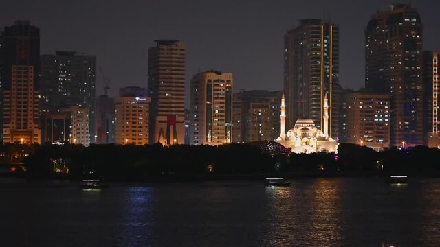 Night view of the iconic Sharjah's Al Noor Mosque, Khalid lake and Al Noor island Sharjah city skyline in the background, tourist boats in the sea, United Arab Emirates, 4K video