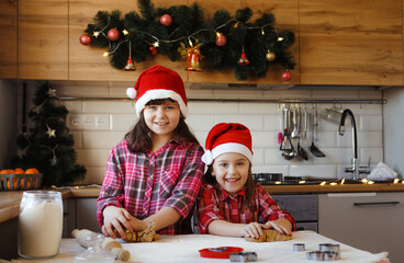 two teenage girls in Christmas hats are making ginger cookies out of dough and laughing merrily