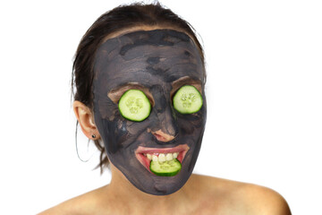 Beautiful girl with a cosmetic mud mask and cucumbers on her eyes.