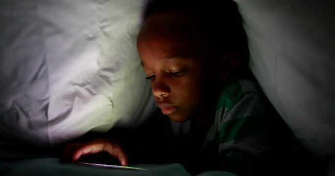 Young boy looking at cellphone screen at night under blanket