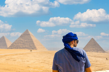 A young tourist wearing blue turban and sunglasses enjoying the Pyramids of Giza, the oldest Funerary monument in the world. In the city of Cairo, Egypt