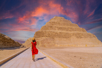 A young tourist in a red dress at the Stepped Pyramid of Djoser at sunset, Saqqara. Egypt. The most...