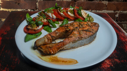 Caprese salad with cherry tomatoes, mozzarella toast and grilled salmon fish on the red brick wall background. Healthy eating concept.
