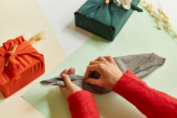 Young female wrapping a zero waste brown gift wrapped in traditional Japanese Furoshiki style in a...