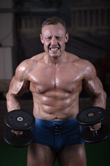 Fototapeta na wymiar A man goes in for sports in the gym and trains his muscles. Bodybuilder works out with dumbbells