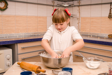 Cute funny girl learns to prepare Christmas gingerbread cookies in bright cozy kitchen, kneads...