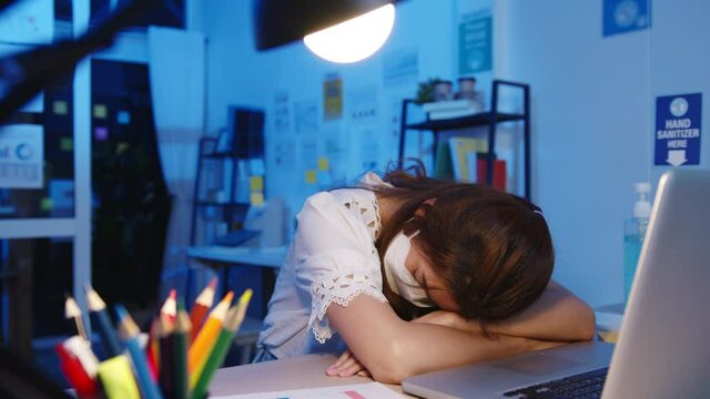 Freelance Asia exhausted lady wear face mask sleeping at new normal home office. Working from house overload at night, Remotely, self isolation, social distance, quarantine for corona virus prevention