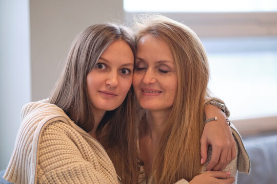 Mother And Grown-up Adult Daughter Sit On Couch In Living Room Have Fun Talking, Happy Mature Mom And Millennial Girl Child Relax On Sofa At Home Together, Chat And Laughing