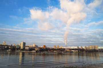 from boiler room tube goes white steam, smoke into sky. Cityscape by river