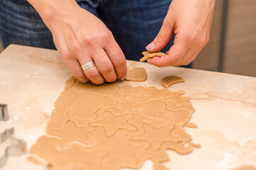 Female hands prepare festive gingerbread cookies for christmas, she rolled out dough and cut cookies with cookie cutters