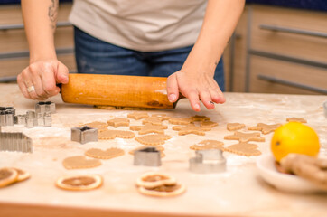 Female hands prepare festive gingerbread cookies for christmas, she rolled out dough and cut cookies with cookie cutters