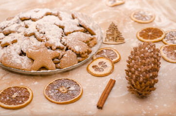 Festive Christmas still life in kitchen, gingerbread cookies with powdered sugar, dried oranges, cone, cinnamon stick