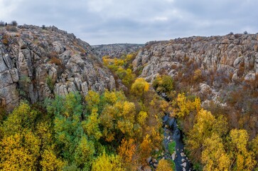 A picturesque stream flows in the Aktovsky Canyon, surrounded by autumn trees and large stone boulders