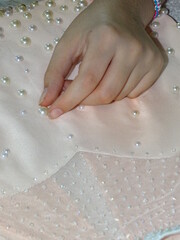 mano de mujer pegando perlitas en un vestido de fiesta color rosado